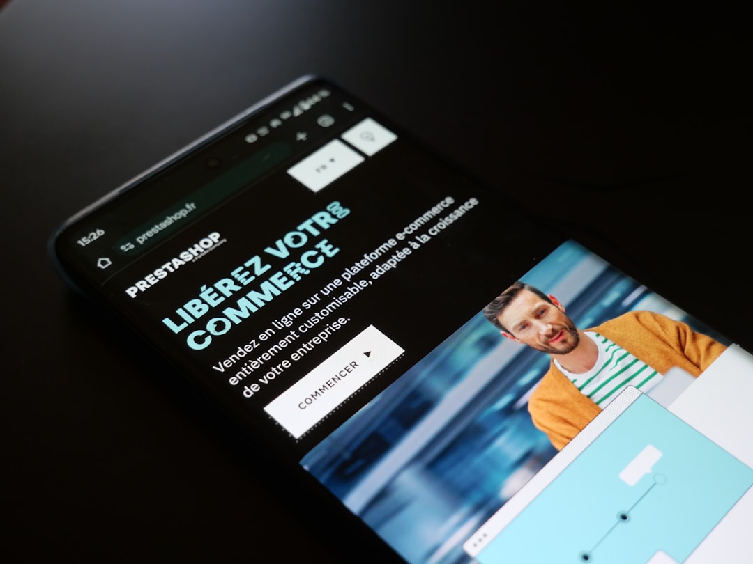 Un smartphone affiche la page de Prestashop avec le slogan Libérez votre commerce. Un homme souriant en fond, un design moderne et un bouton d’action incitent à explorer la plateforme e-commerce